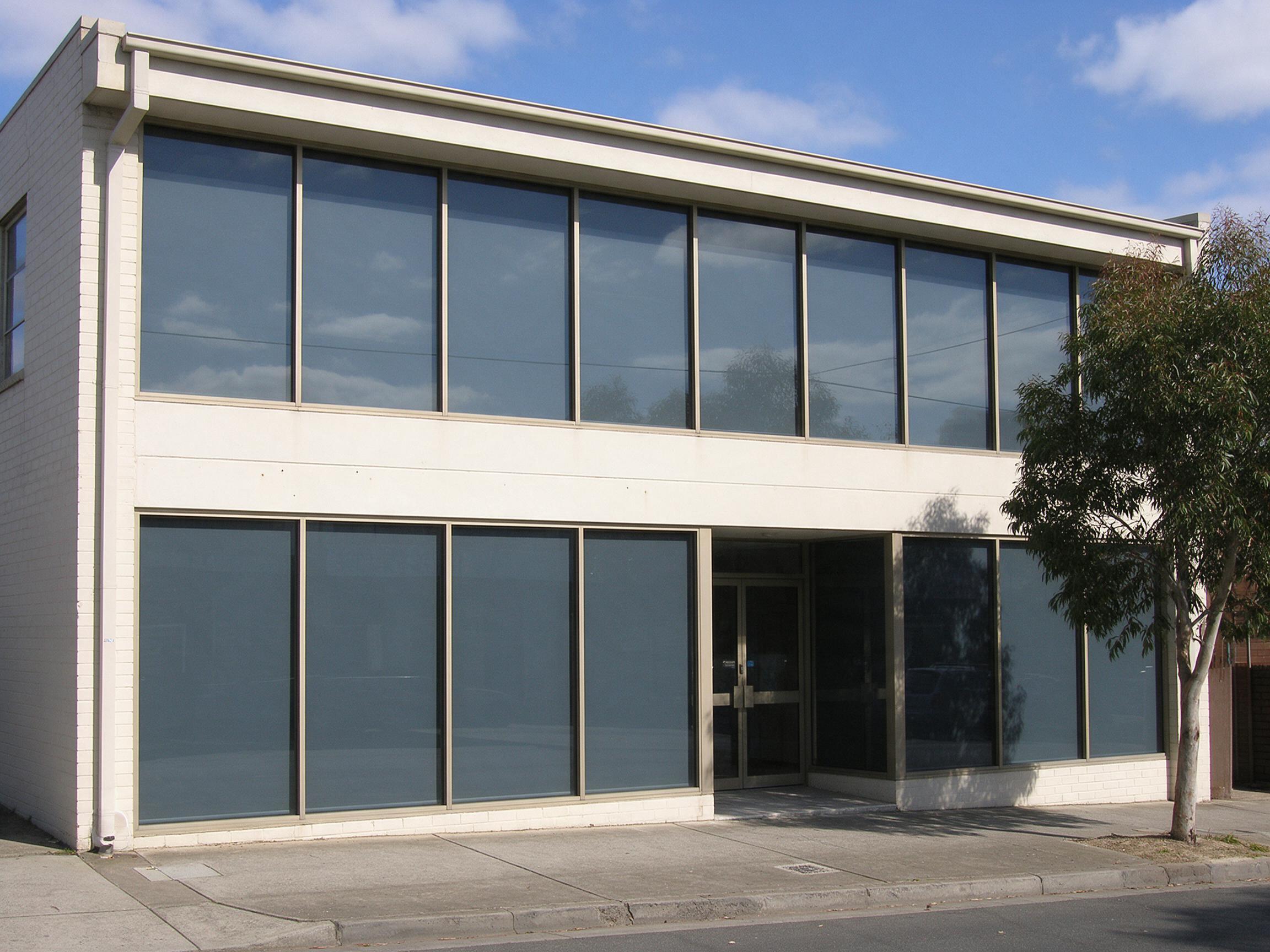 A two storey commercial building with solar film across the whole street facade, every pane the same restrained tone and the sky reflected in the upper band