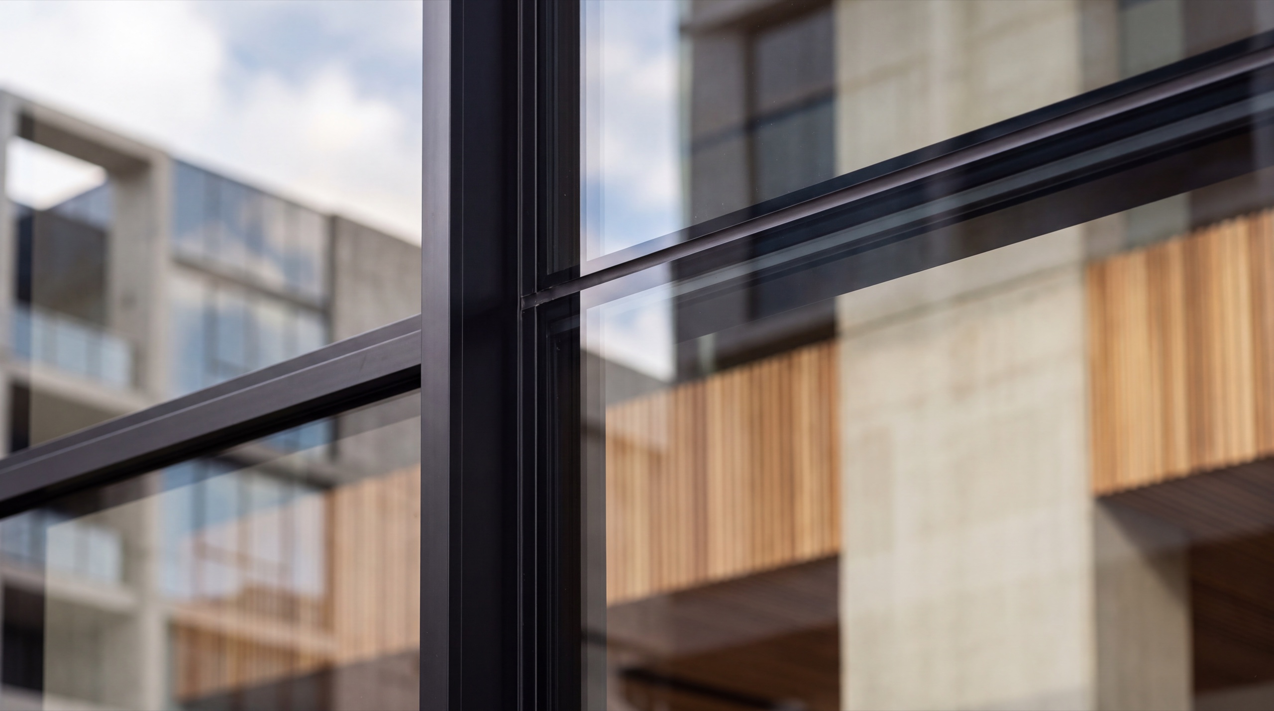 A close raking view of one glazing bay on a commercial building, the neighbouring facade reflected in the glass