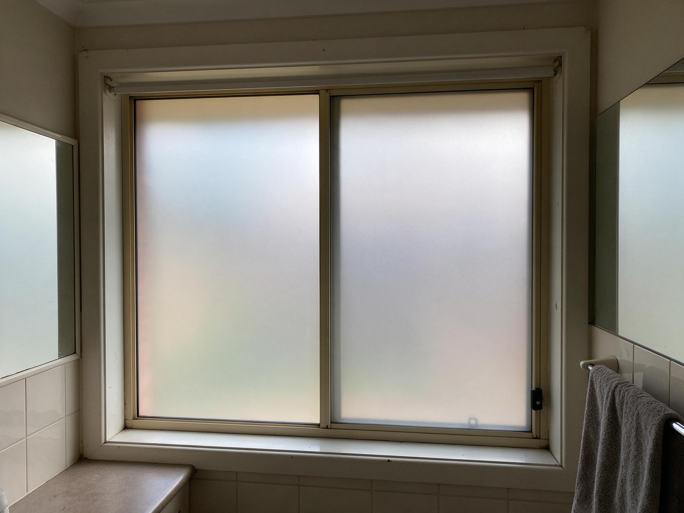 A sliding bathroom window with frosted film across both sashes, the garden outside reduced to soft colour and daylight still filling the room