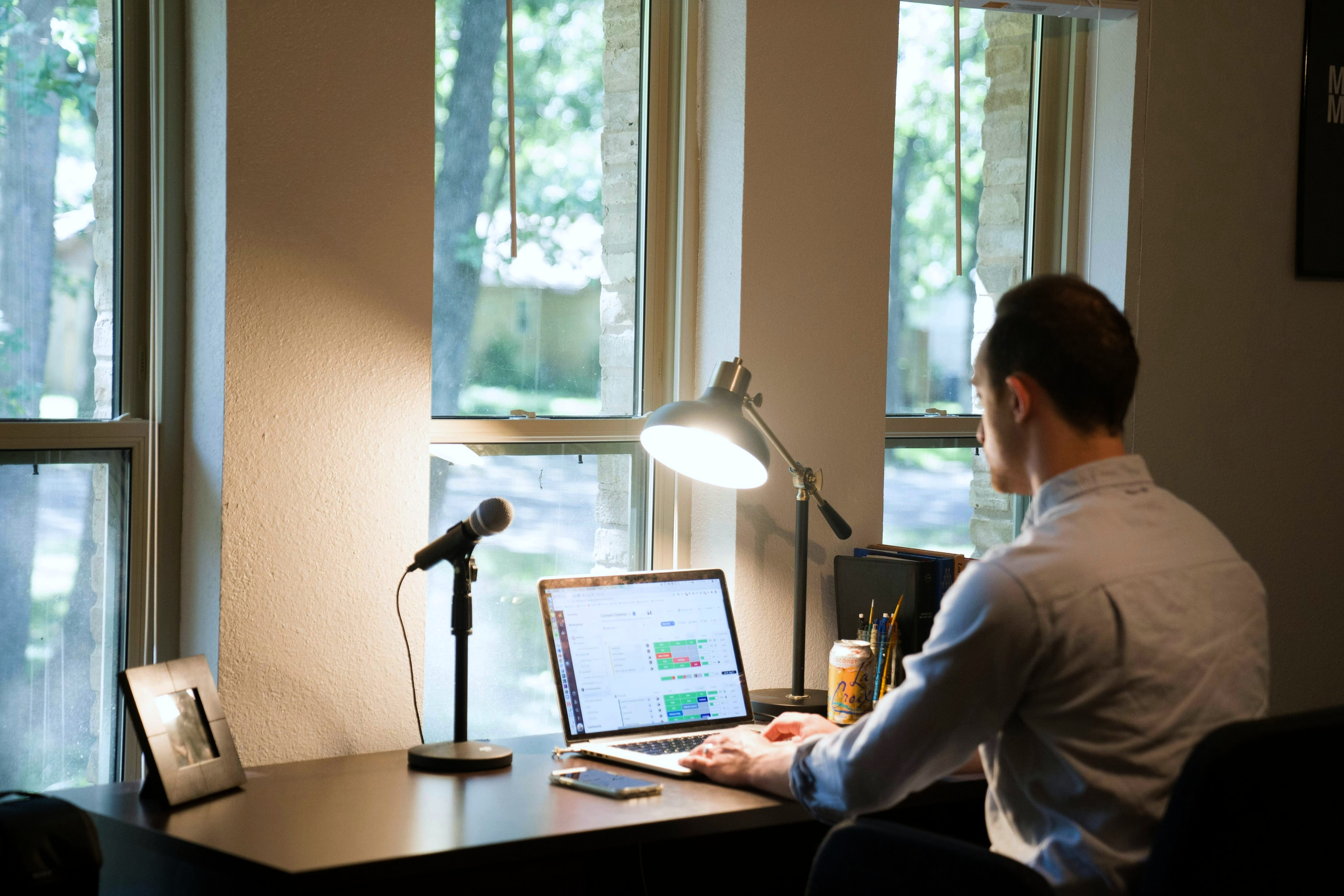 A desk beside tall windows with a laptop screen legible against the daylight behind it