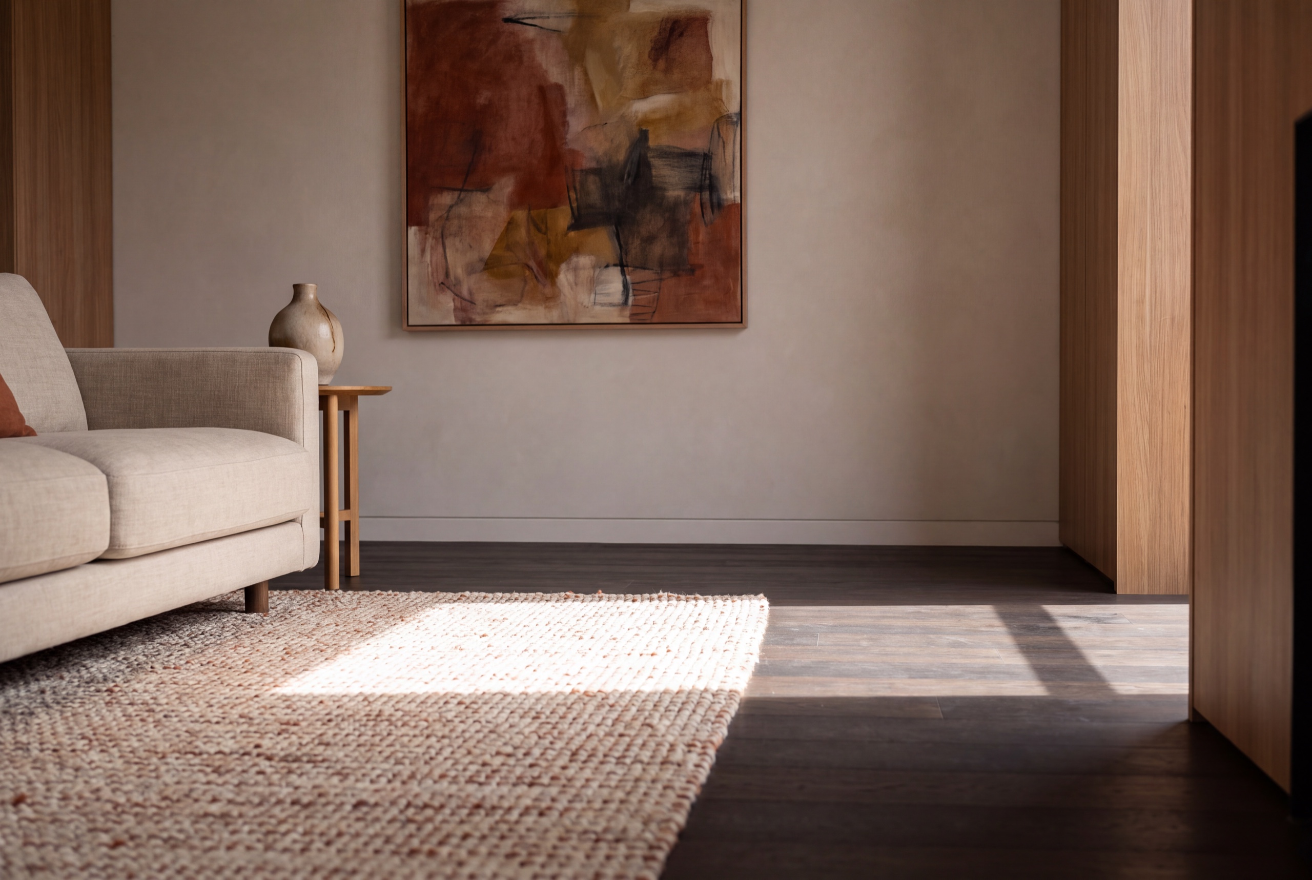 Late morning sun falling in a window shaped patch across a jute rug and a dark timber floor, beneath a framed artwork with its colour intact